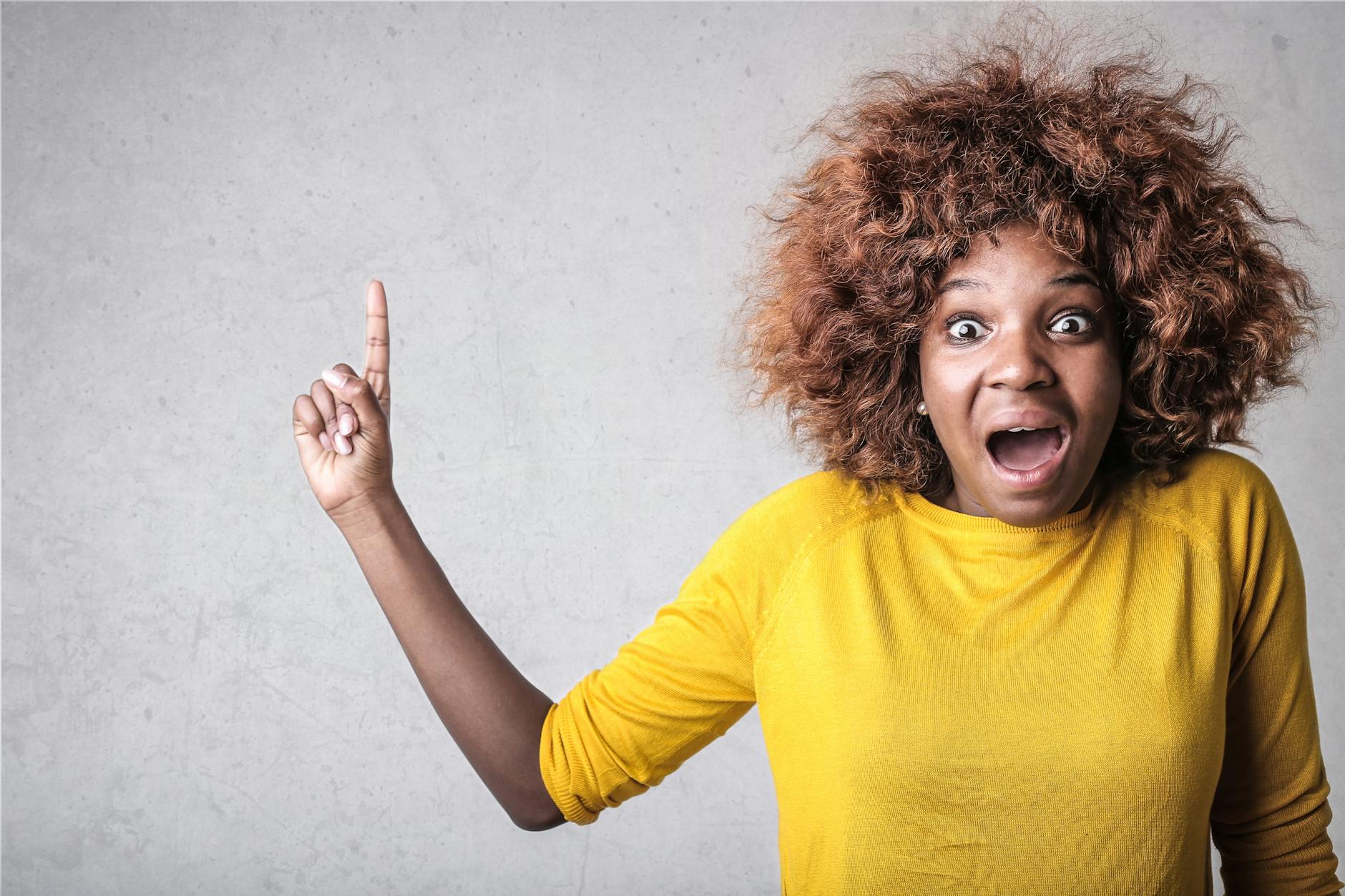 Portrait of a joyful woman pointing upwards, expressing excitement in a studio setting.