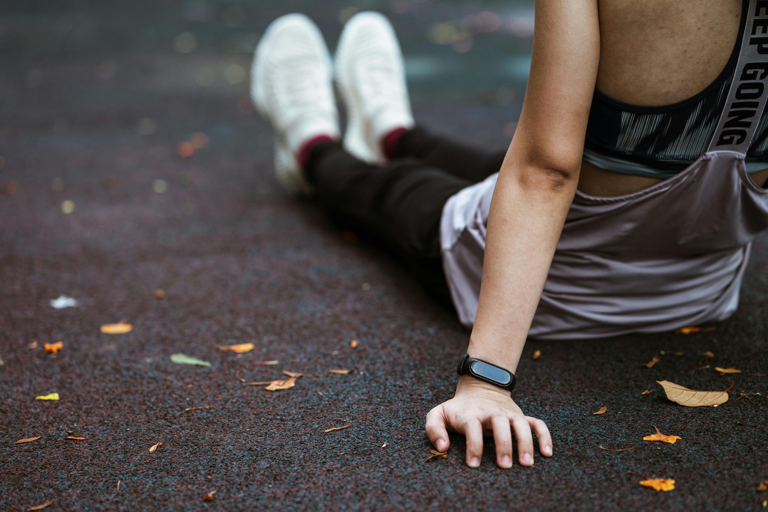 A woman in activewear rests on a track, using a smartwatch to track workout progress.